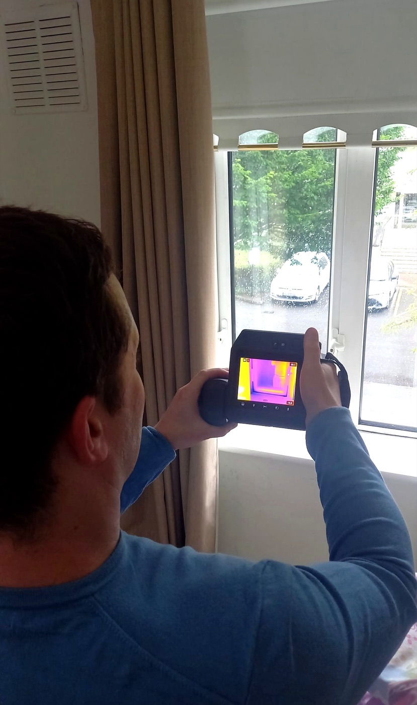 Dave from HeatCheck using a FLIR thermal camera to inspect a window during a home energy survey